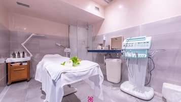 Un baño moderno con ducha de vidrio, lavamanos blanco y una mesa de masajes con un arreglo floral.
