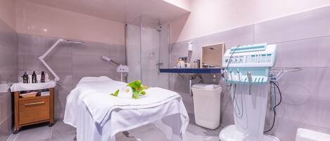 A modern bathroom with a glass-enclosed shower, a white sink, and a massage table with a flower arrangement.