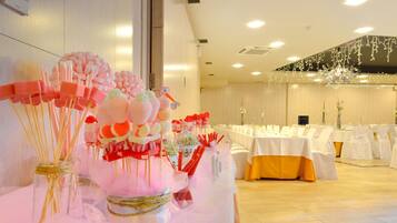 Une salle de banquet où les tables sont dressées pour un événement formel, décorée de compositions florales et d’un lustre.