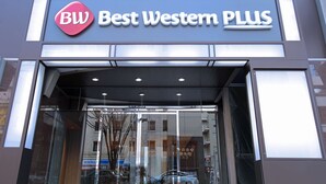 Entrada de un hotel Best Western Plus con fachada de vidrio transparente, un logotipo destacado y un diseño arquitectónico moderno.