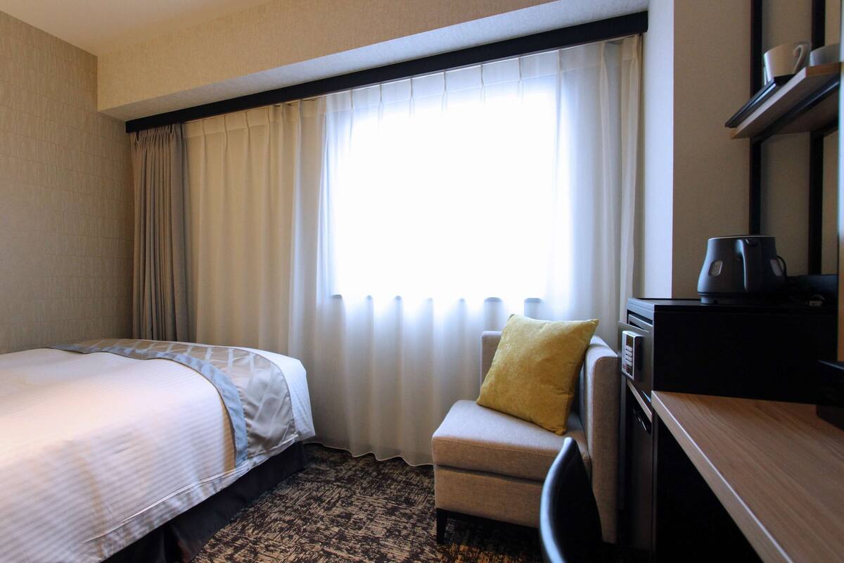 Habitación de hotel con cama, escritorio, silla y ventana con cortinas.