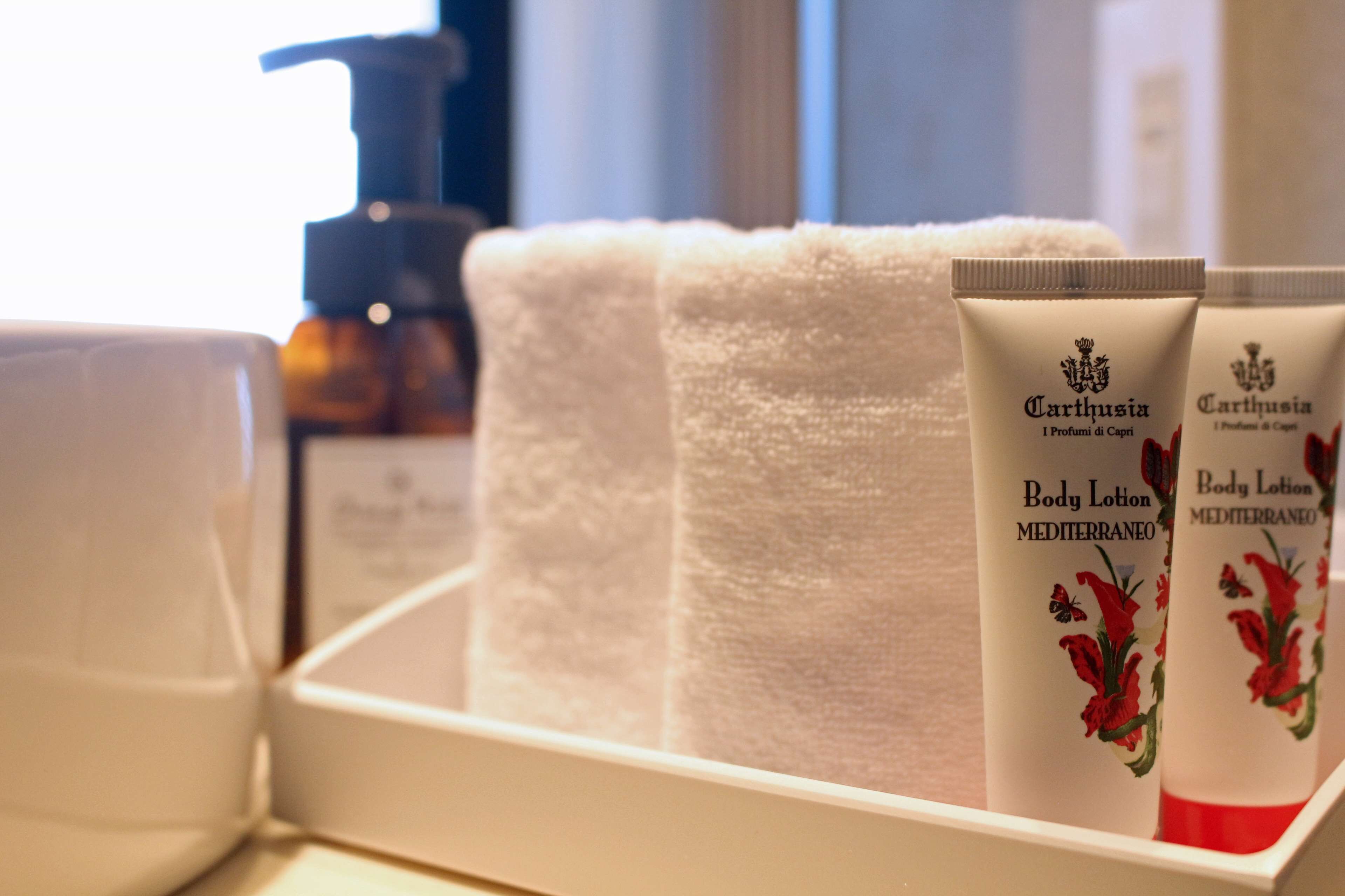 A bathroom with a white towel, two body lotion tubes, and a soap dispenser.