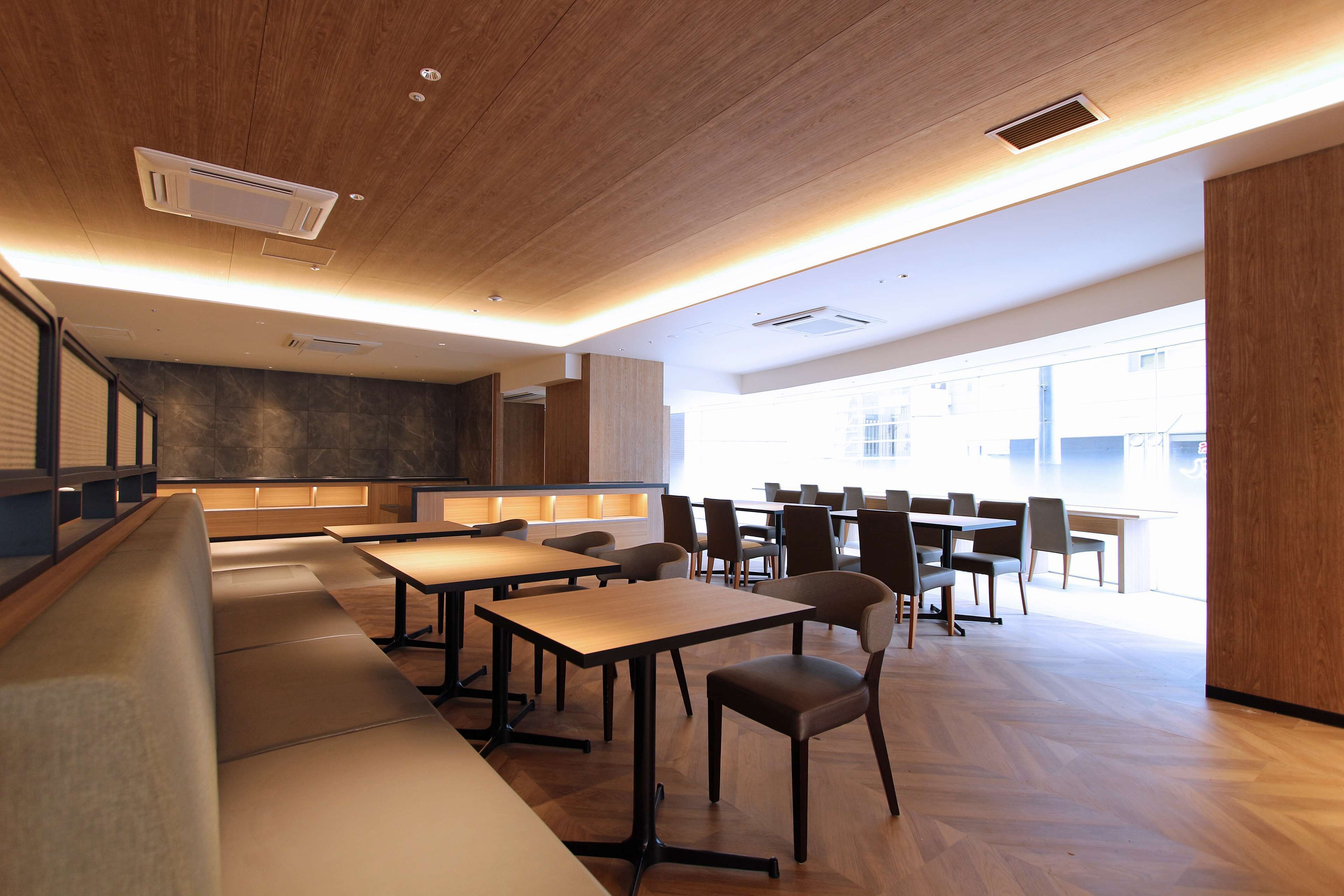 A modern dining area with wooden flooring, long tables, and cushioned seating.