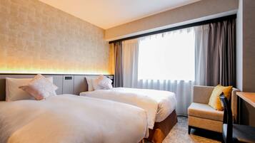 A hotel room with two beds, a small armchair, and a large window with curtains.