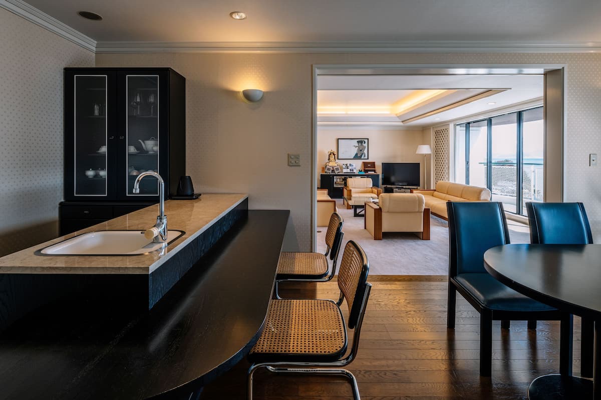 A modern hotel room with a kitchen area, dining table, and seating.