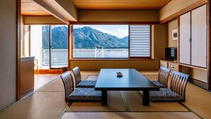 A traditional Japanese room with tatami flooring, a low table, and chairs, a sliding door, and a view of mountains. - Aki Grand Hotel & Spa (Hatsukaichi)