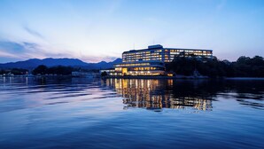 A multi-story hotel with a modern design, situated by a calm body of water with mountains in the background. - Aki Grand Hotel & Spa (Hatsukaichi)