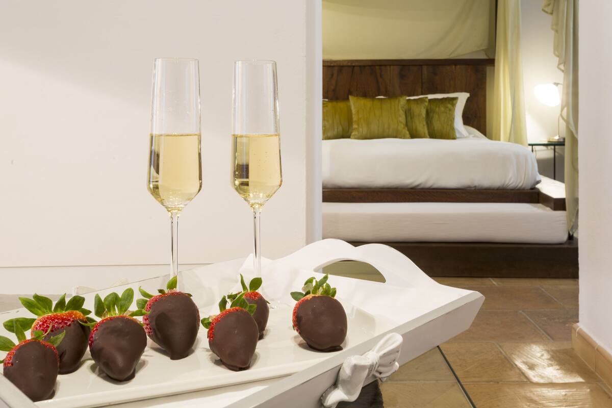 Een schaal met chocoladebedekte aardbeien en twee glazen witte wijn op een witte tafel.
