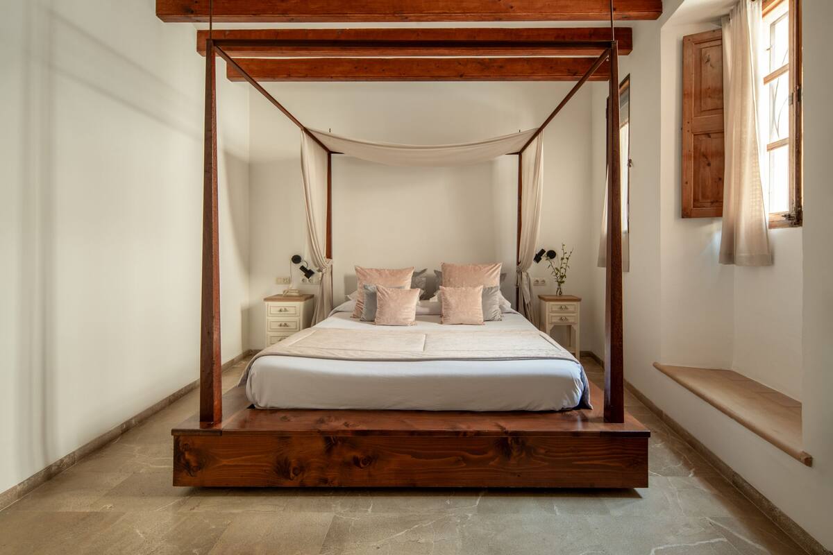 Een slaapkamer met een hemelbed, houten hoofdbord en een stenen vloer.
