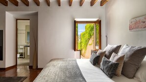 Een slaapkamer met een groot bed, houten balken, een raam met uitzicht op groen en een schilderij aan de muur.
