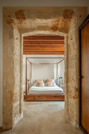 A bedroom with a four-poster bed, stone walls, and a wooden ceiling. - Hotel Can Joan Capó - Adults Only (Sineu)