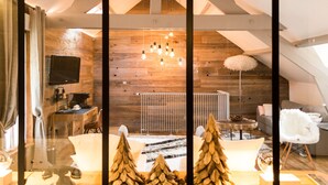 Una habitación acogedora y bien iluminada, con paredes de madera, una lámpara moderna y una zona de estar cómoda con una silla blanca y un sofá.
