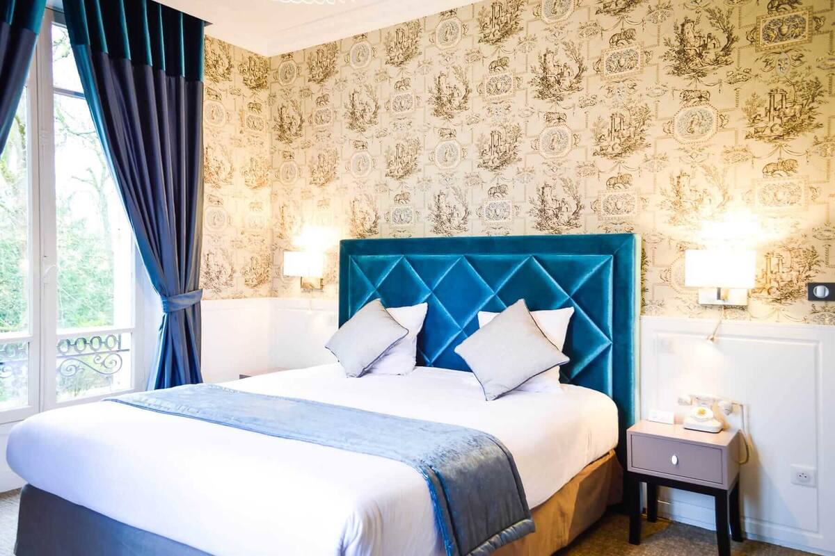 A hotel room with a large bed, two bedside tables, and a window with curtains.