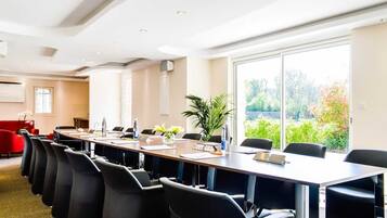Ein Konferenzraum mit einem langen Tisch, schwarzen Stühlen und einem großen Fenster mit Blick auf Grünflächen.