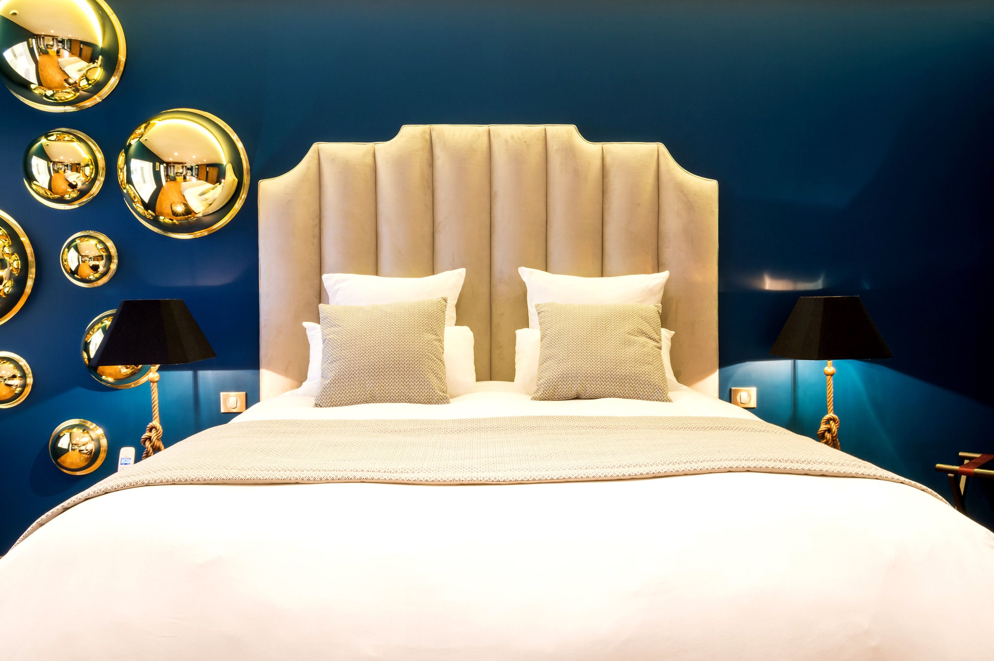 Una habitación de hotel con una cama grande, dos lámparas de noche y varios espejos en la pared.