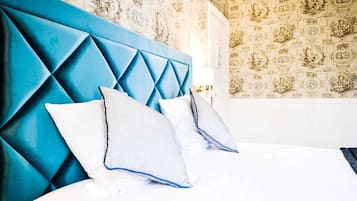 A bed with a blue headboard and two pillows, a patterned wallpaper, and a white door.
