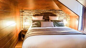 Un dormitorio con pared de piedra, cama con ropa de cama blanca y dos lámparas de noche.