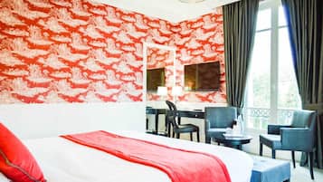 A hotel room with a large bed, a desk with two chairs, a TV, and a window with curtains.