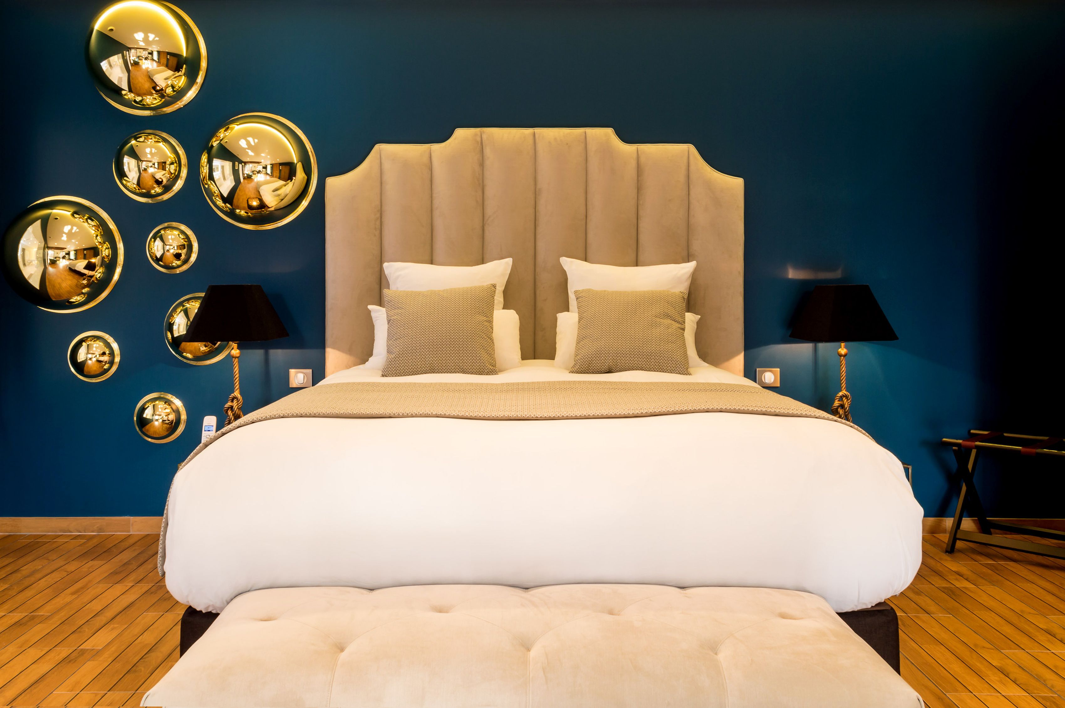 Ein großes Bett mit einer gepolsterten Kopfteile, zwei Nachttische mit Lampen und eine Reihe von wandmontierten Spiegeln.