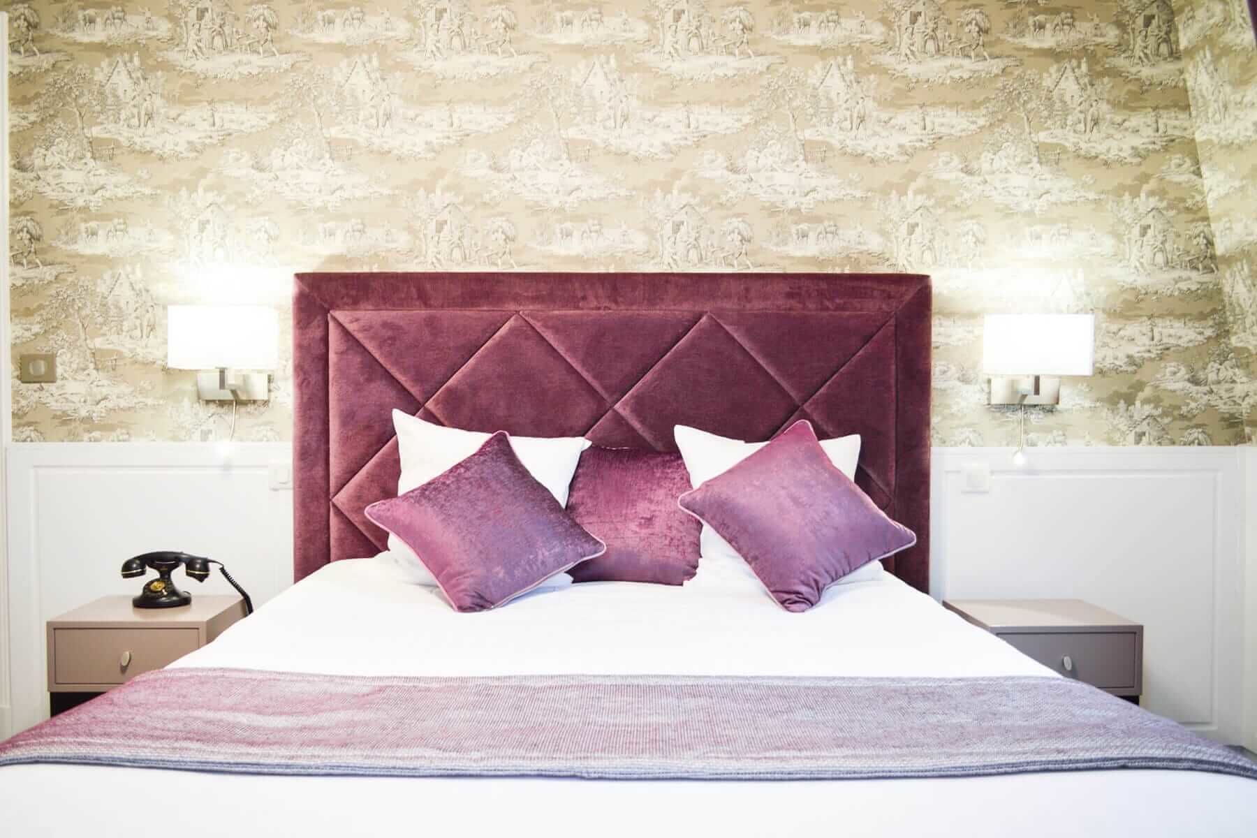 A bed with a tufted headboard, white bedding, and purple pillows.