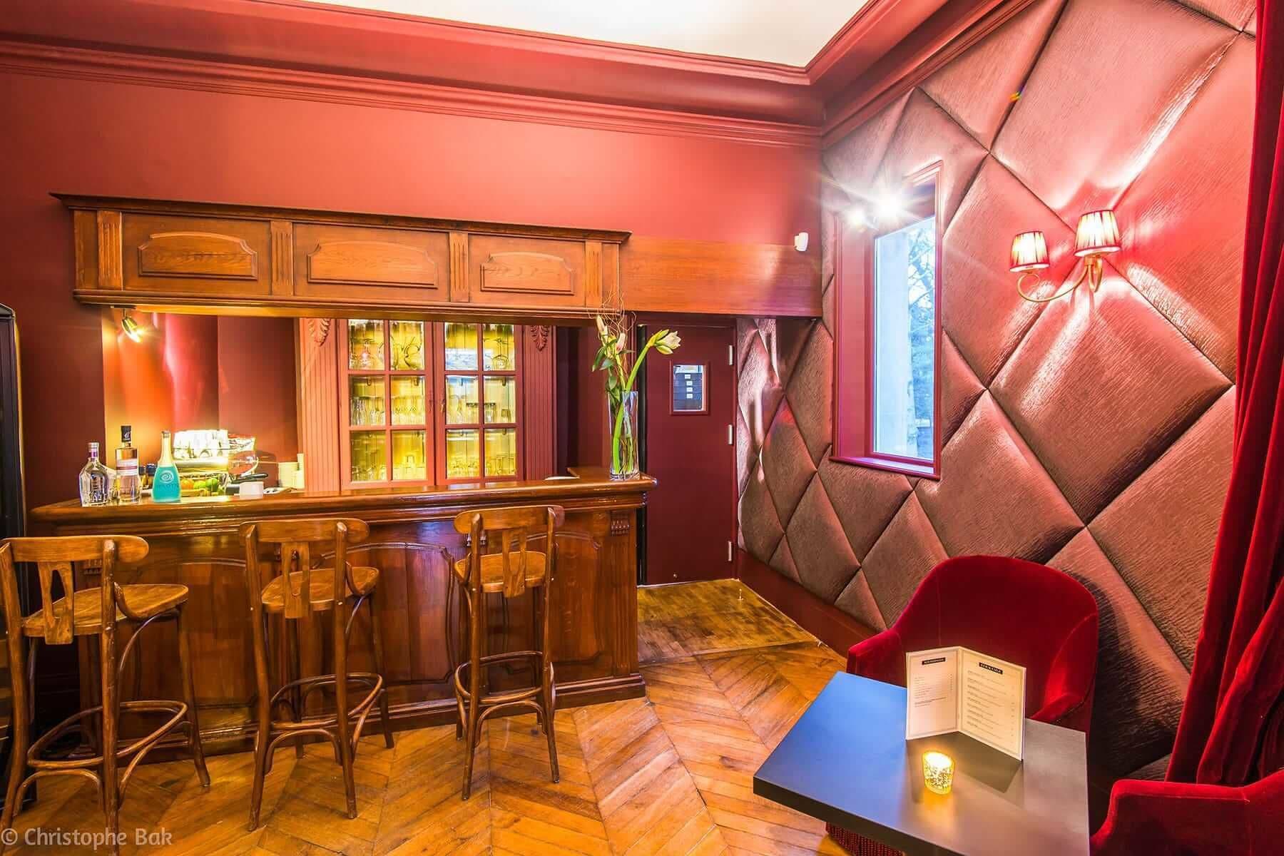 Un espace bar avec des chaises en bois, un comptoir et un coin salon rouge avec des coussins, ainsi qu’un menu.