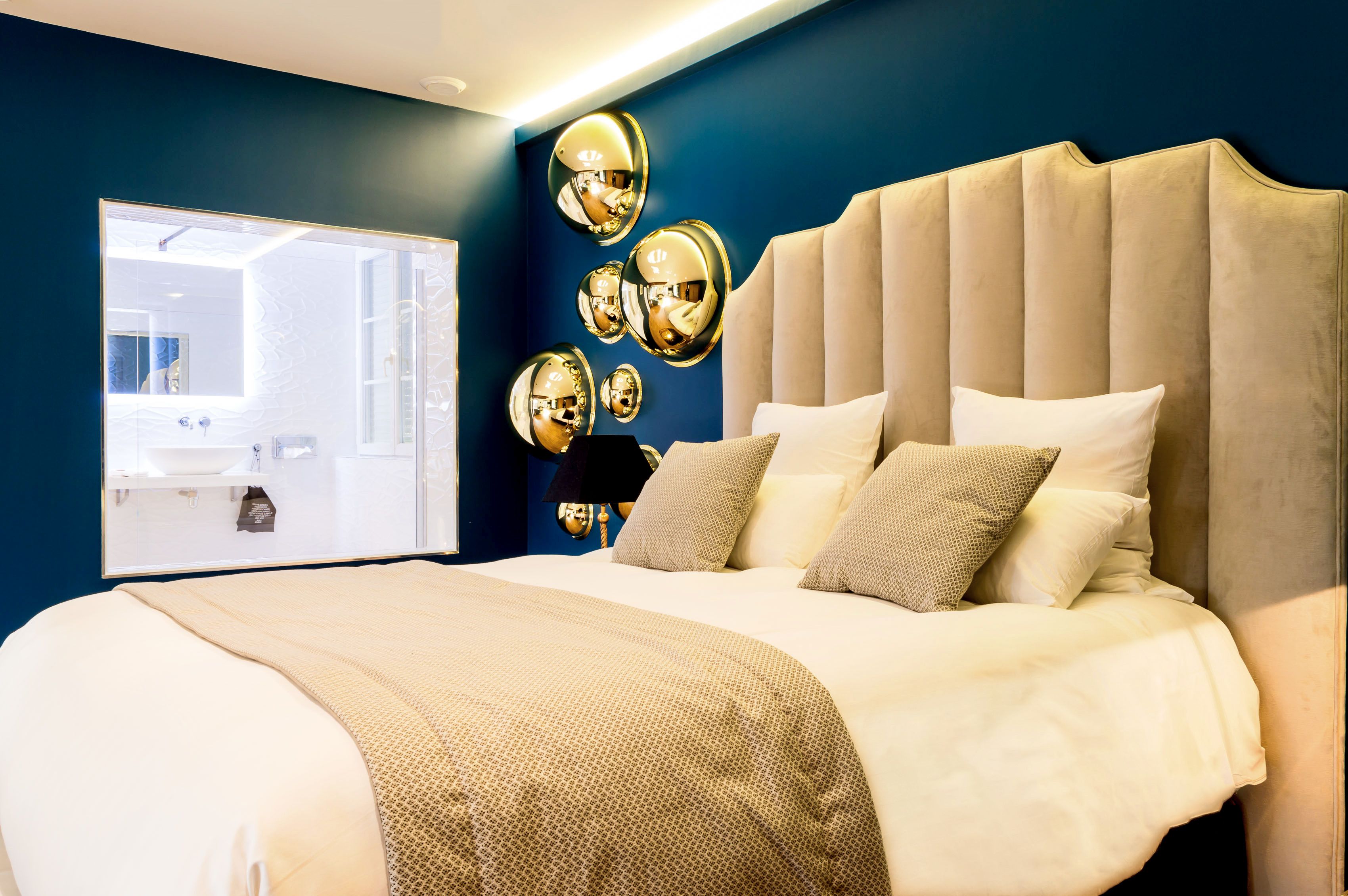 Une chambre à coucher moderne avec un grand lit, une tête de lit capitonnée et un miroir doté de plusieurs surfaces réfléchissantes.