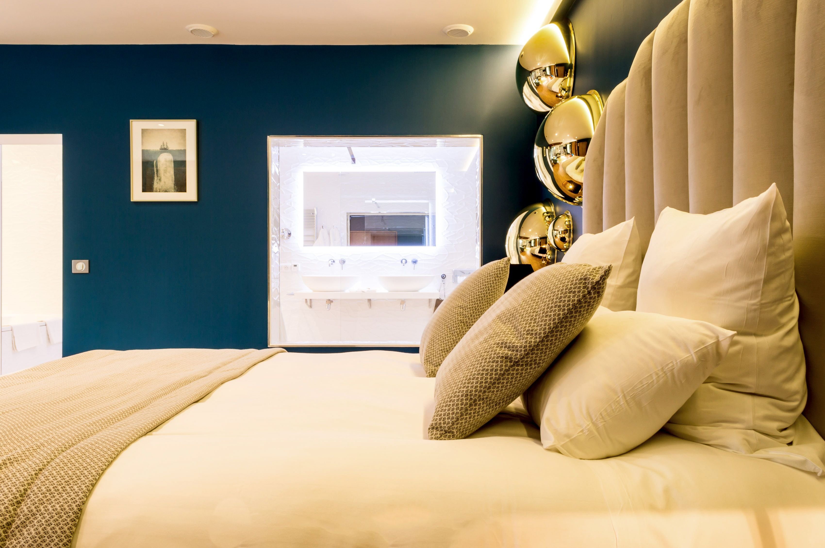 A bedroom with a large bed, a window with a view, and a wall-mounted mirror.