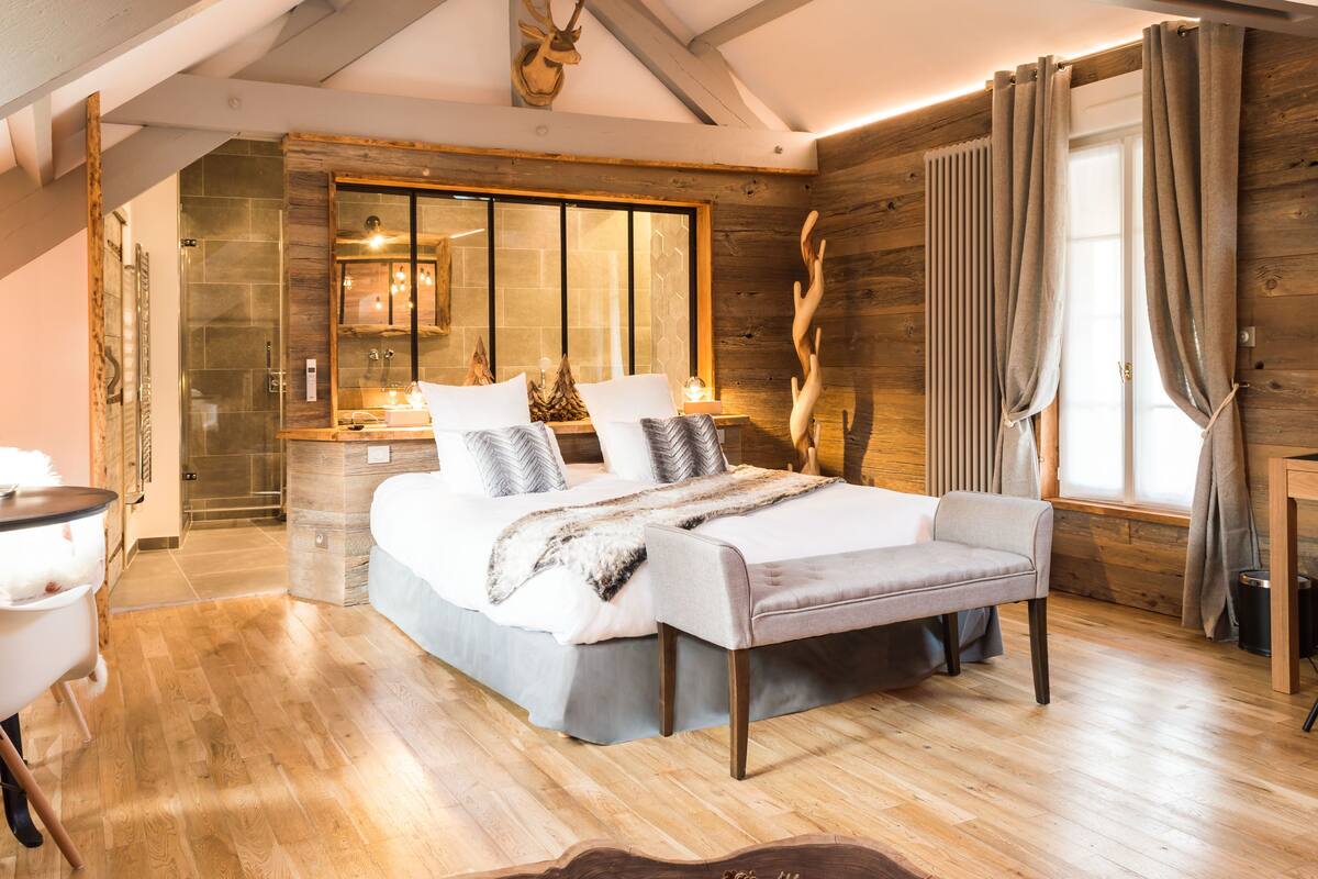 A modern bedroom with a large bed, wooden walls, a built-in bench, and a view of the outdoors.