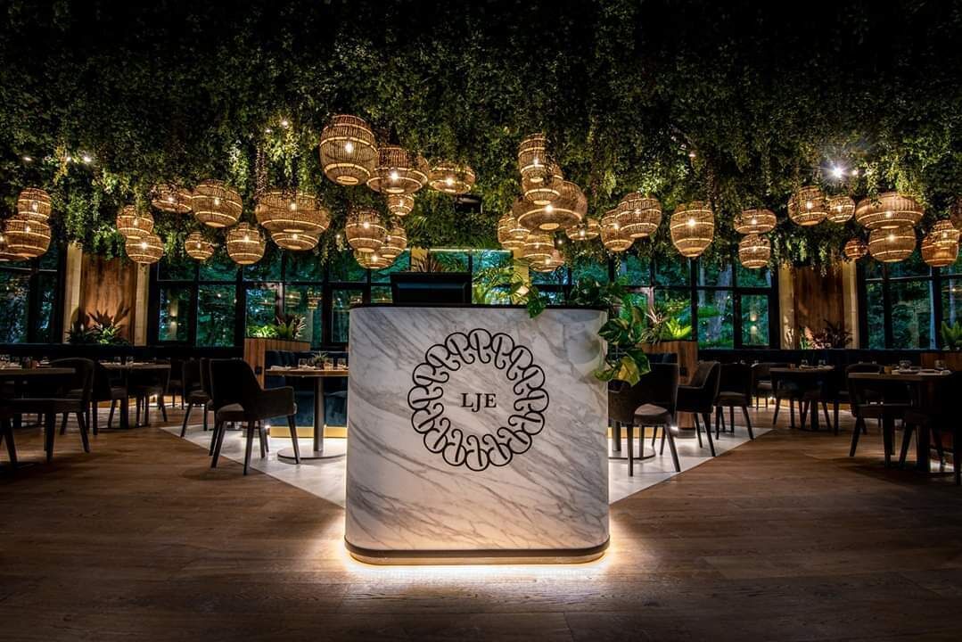 Een restaurantinterieur met een marmeren toonbank, hangende wilgentaklampen en weelderige begroeiing.