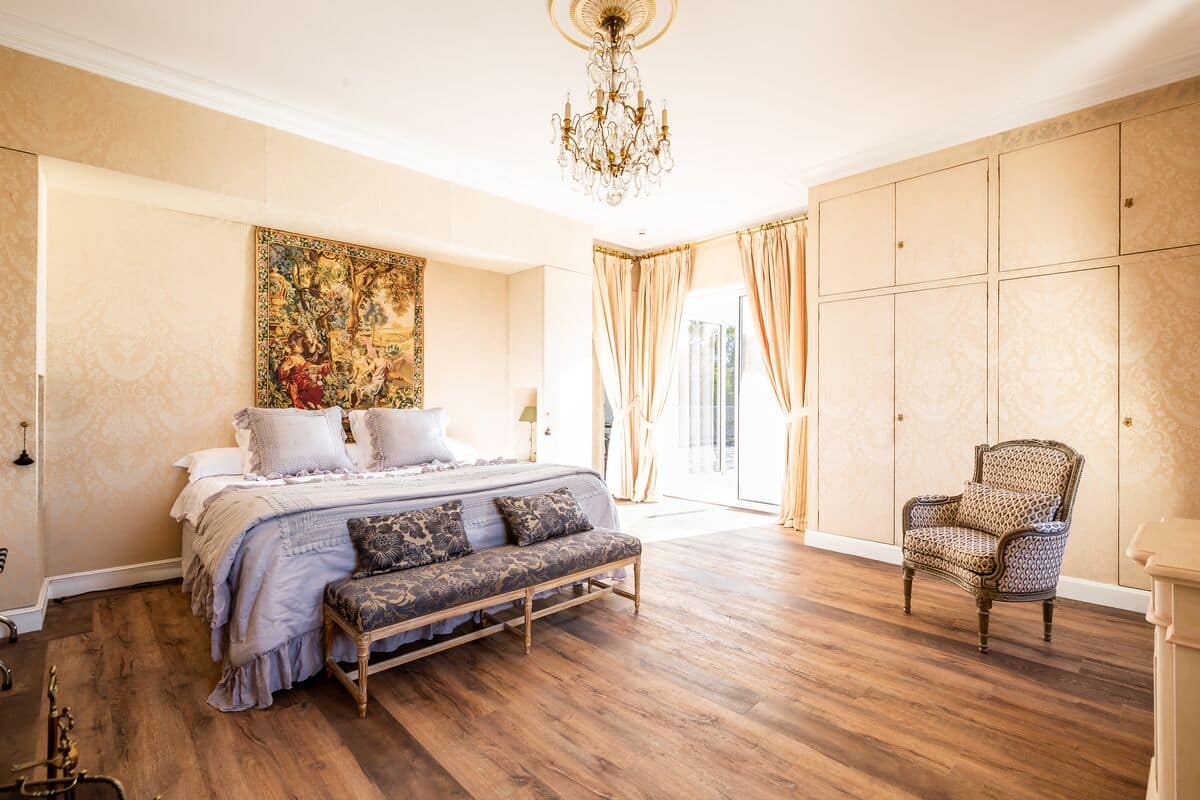A bedroom with a large bed, a bench, a chair, and a chandelier.