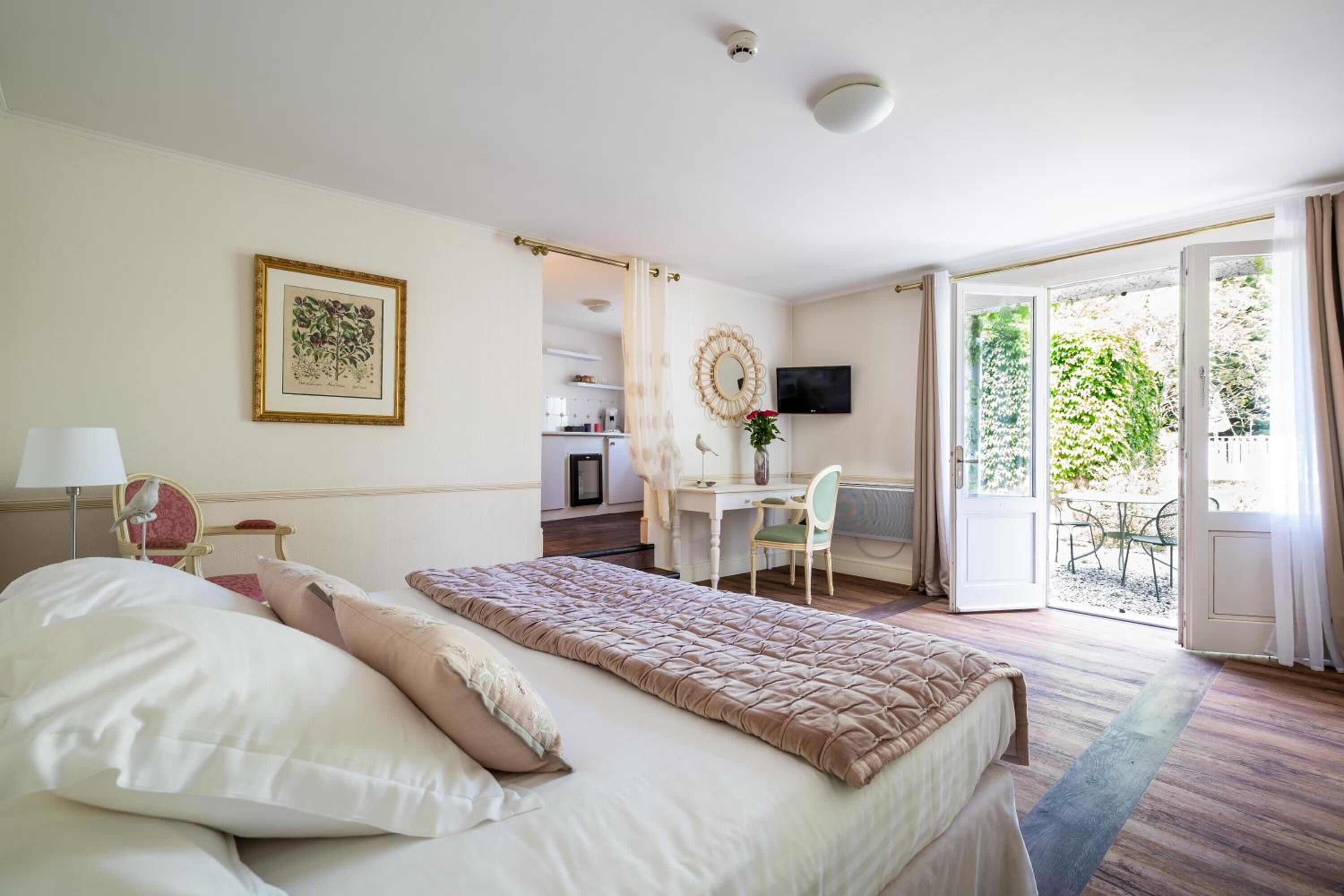 A hotel room with a bed, a desk, a chair, a TV, and a balcony with a view of greenery.