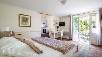 A hotel room with a bed, a desk, a chair, a TV, and a balcony with a view of greenery.