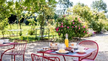 An outdoor dining area with red metal chairs and a table set for breakfast.