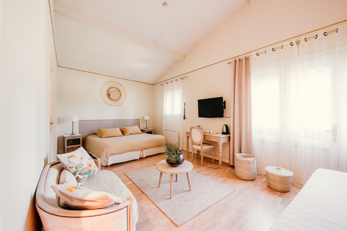 A bedroom with a bed, bedside tables, a desk, a chair, a television, and a window with curtains.