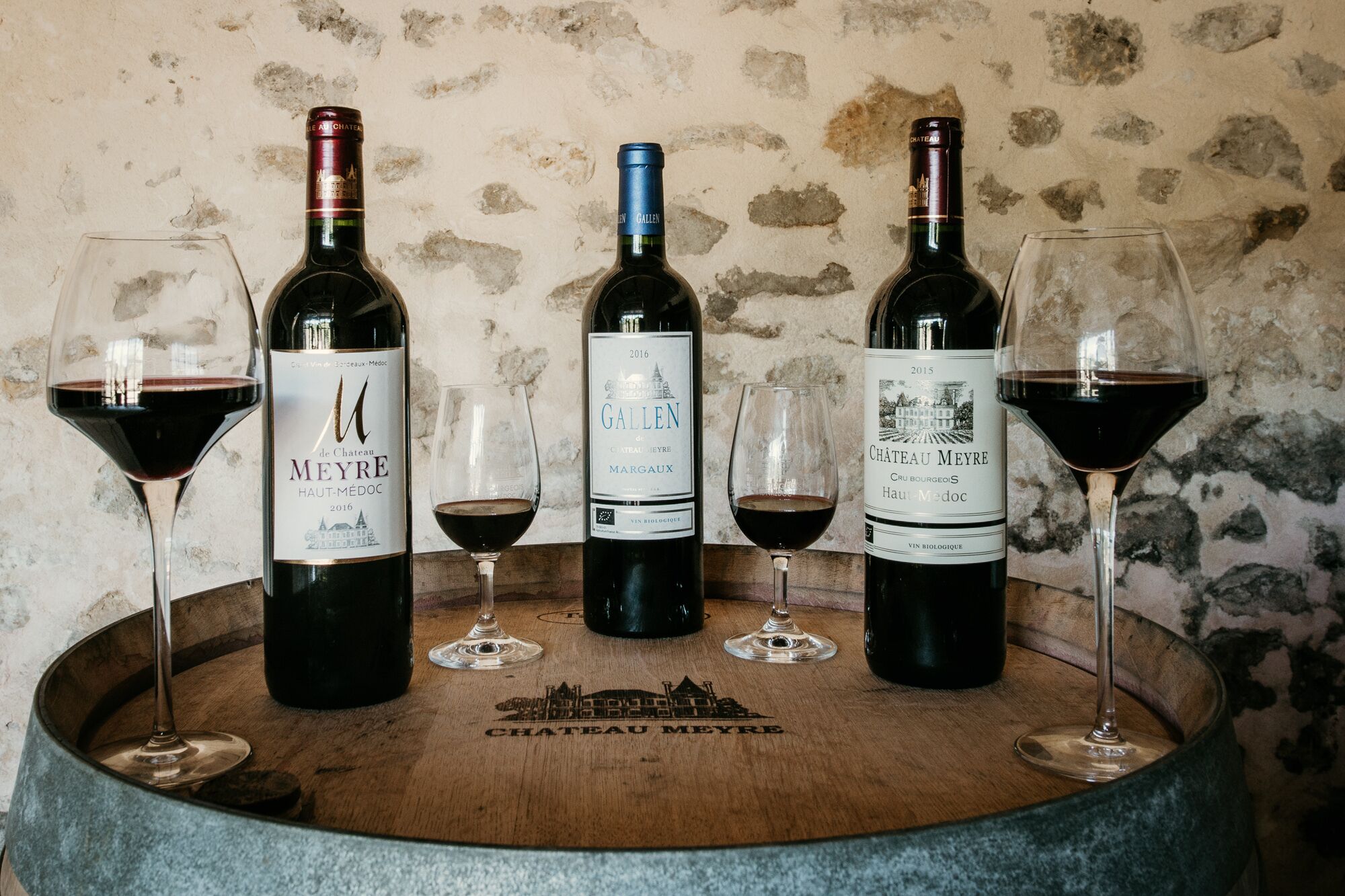 Four wine bottles with glasses on a wooden barrel labeled "CHATEAU MEYRE".