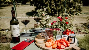Un montaje para picnic con una botella de vino, copas, varios quesos, frutas y una tabla de madera.