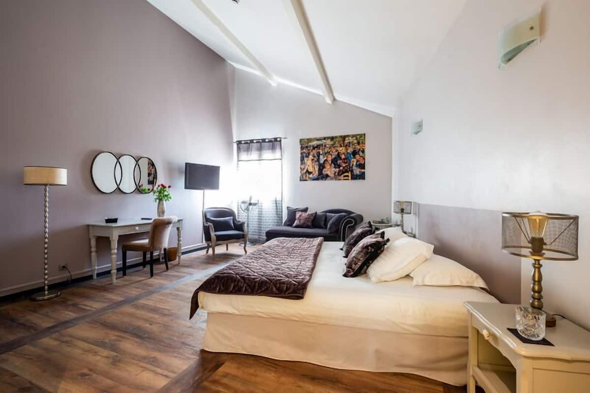 A bedroom with a bed, bedside table, lamp, desk, chair, and a television.