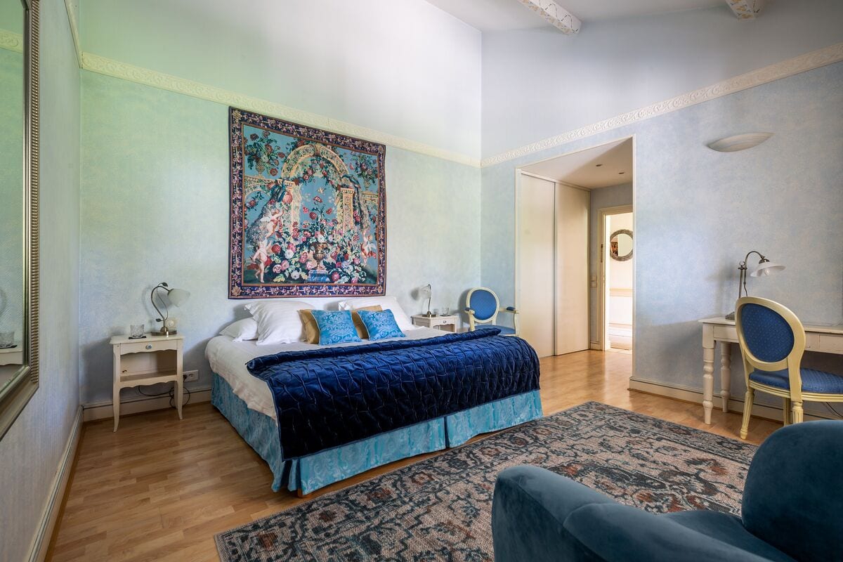 A bedroom with a large bed, a desk, a chair, and a decorative tapestry on the wall.
