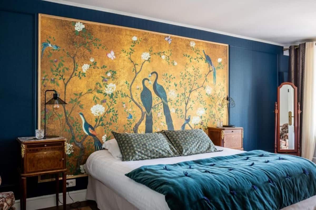 A bedroom with a large floral mural on the wall, a bed with a teal bedspread, and a nightstand with a lamp.