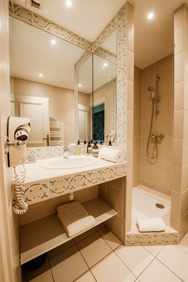 Une salle de bain avec un grand miroir, un lavabo, une douche et un sèche-cheveux.