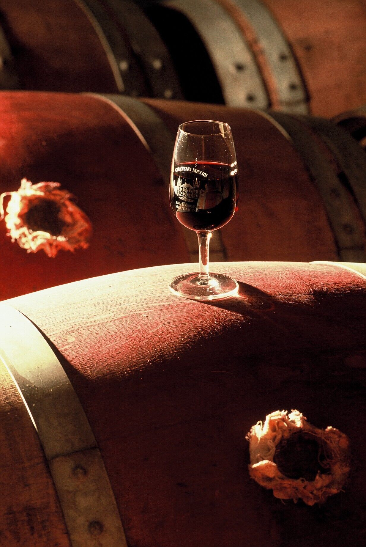 A wine glass on a barrel with a label reading "Chateau Meyre."