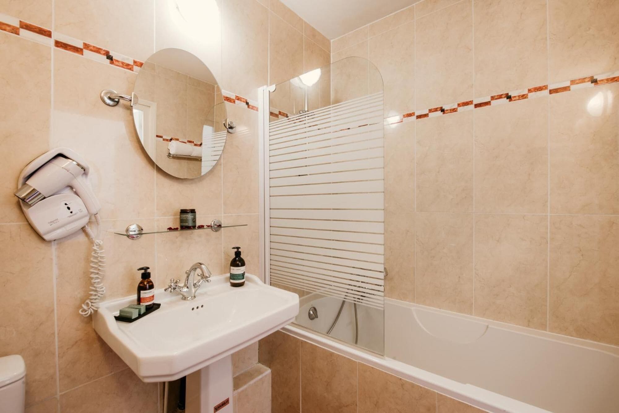 Un baño con lavamanos blanco, secador de pelo, espejo y ducha con puerta blanca.