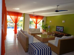 A living room with wicker furniture, a television, and a view of a pool. - Pousada Dos Reis (Búzios)