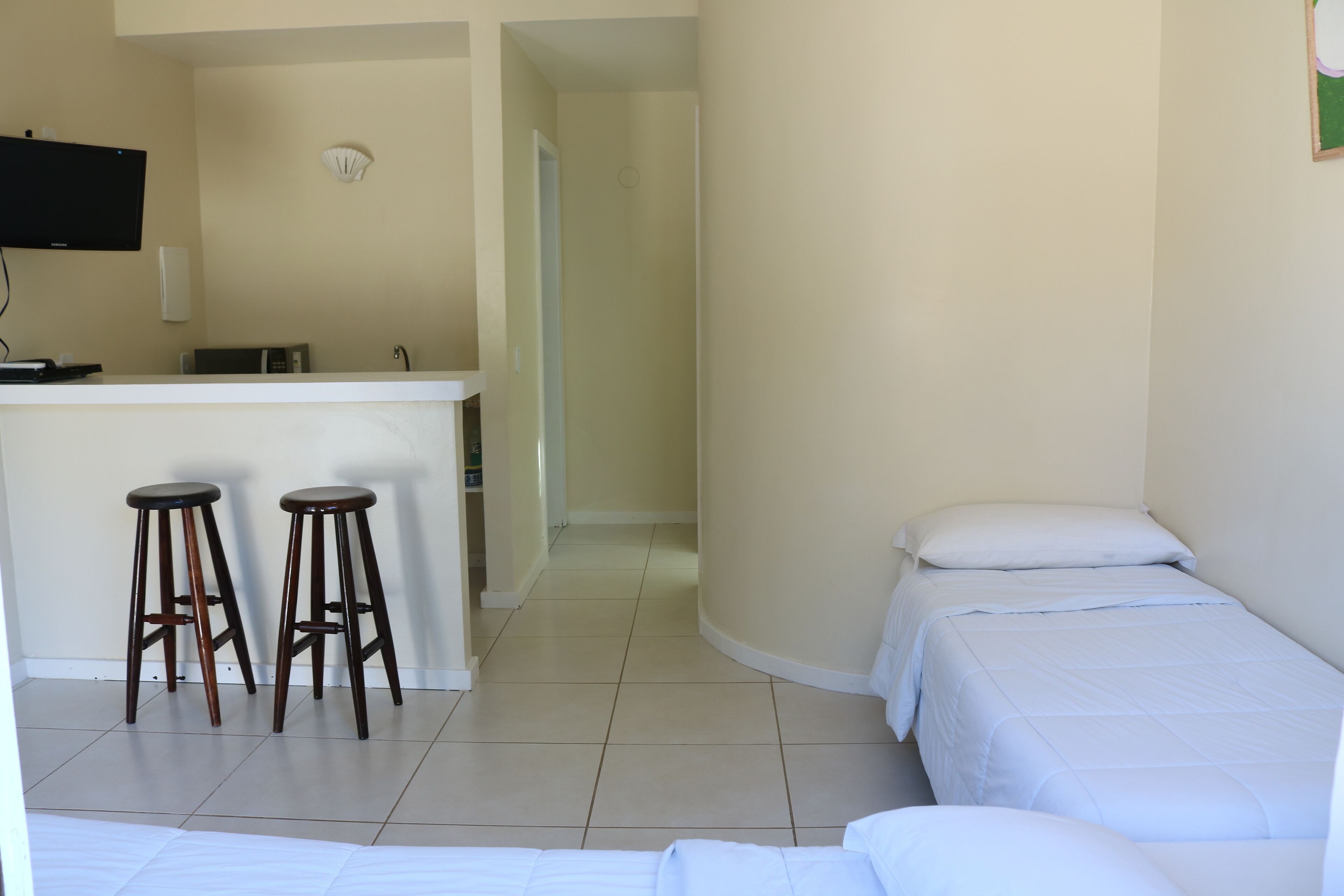 Une chambre d’hôtel équipée d’une kitchenette, de deux tabourets de bar, d’un lit et d’un téléviseur fixé au mur.