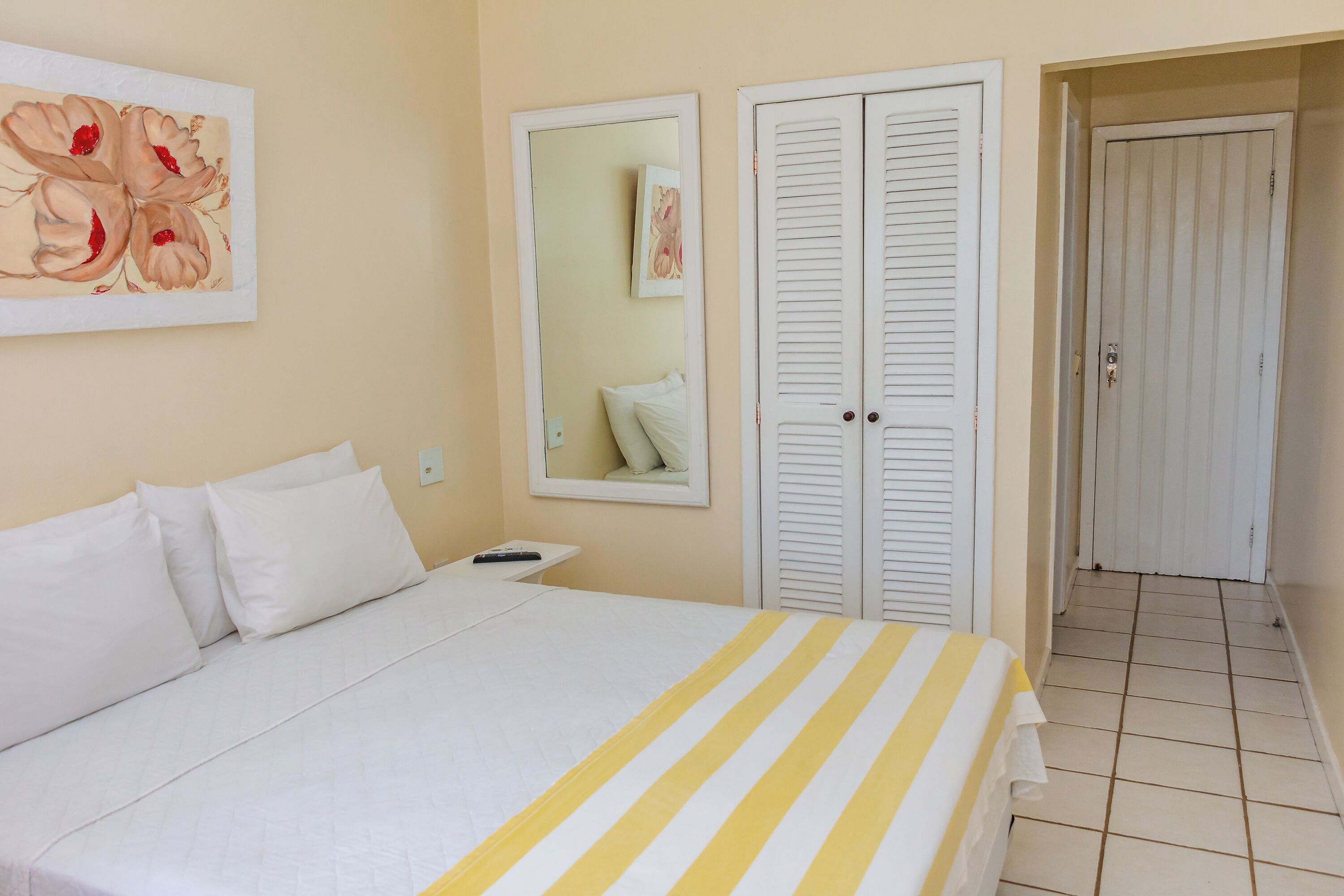A hotel room with a bed, white curtains, a mirror, and a painting on the wall.