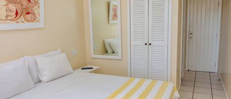 A hotel room with a bed, white curtains, a mirror, and a painting on the wall.