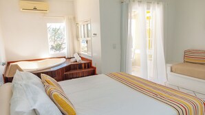 A bedroom with a large bed, a wooden bench, a bathtub, and a window with curtains. - Pousada Dos Reis (Búzios)