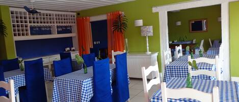 Un restaurante con manteles azules y blancos a cuadros, sillas blancas y paredes verdes.