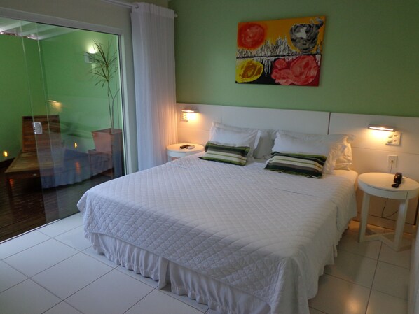 A hotel room with a large bed, two bedside tables, a painting on the wall, and a view of a staircase. - Pousada Dos Reis (Búzios)