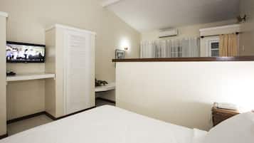A hotel room with a bed, a television mounted on the wall, a wardrobe, a bedside table with a lamp, and a small plant.